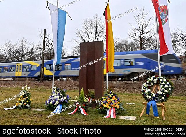 09 February 2021, Bavaria, Bad Aibling: Funeral wreaths and flower arrangements lie at the memorial site. A train passes the memorial for the victims of the...