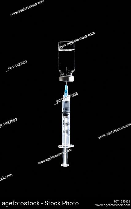 Syringe in COVID-19 vaccine vial on black background