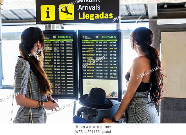 Two fashionable young women at the airport terminal checking the arrival departure board