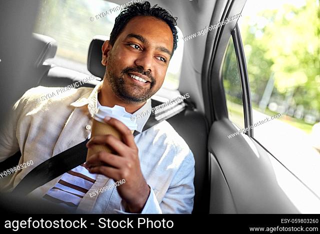 indian man with takeaway coffee on car back seat