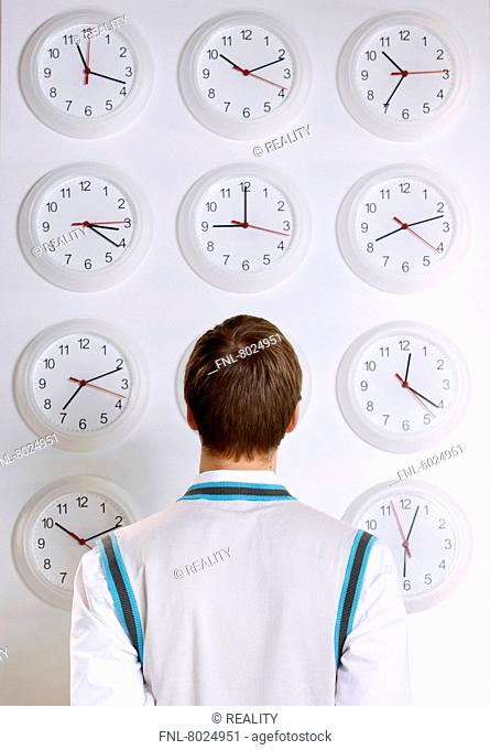 Young man in front of wall with clocks