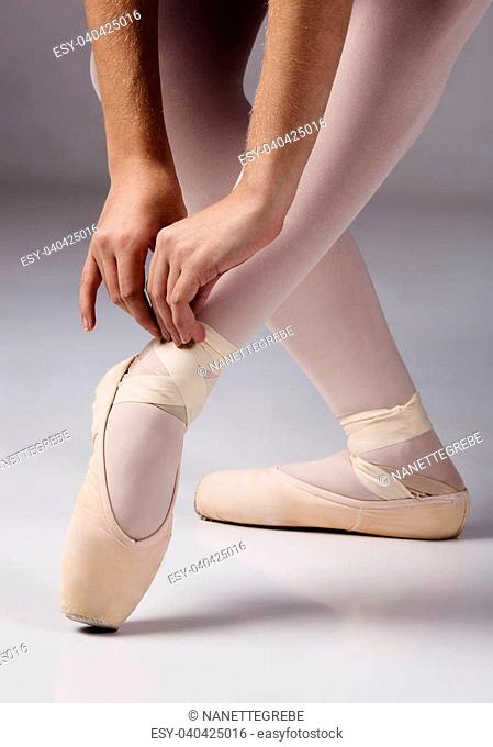 Female ballet dancer tying the ribbons of her pointe shoes