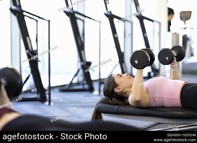 Young woman laying on a weight bench doing arm exercise with 10lb dumbbell