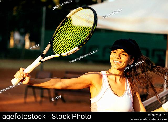 Happy female athlete with racket playing tennis at sports court