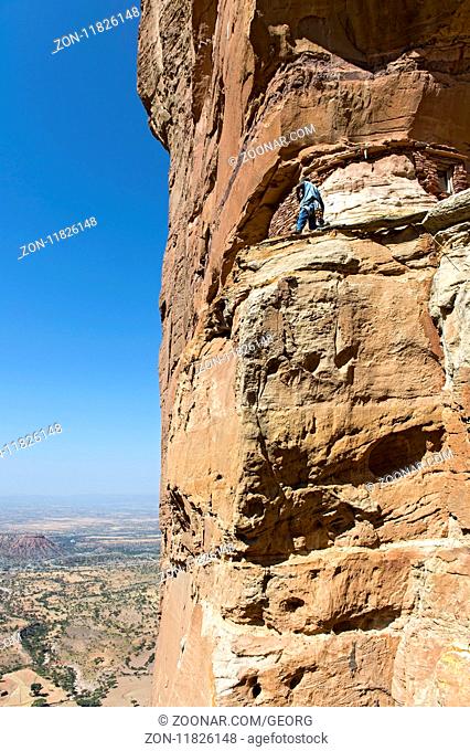 Einheimischer auf einem exponierten Felsband am Eingang zur Felsenkirche Abuna Yemata, Tigray, Ãthiopien / Local on an exposed rock ledge at the entrance to the...