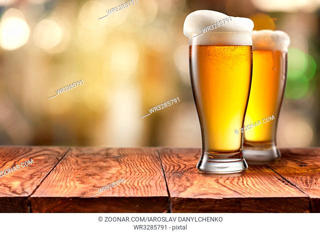 Two Glass of beer with foam on empty brown wooden table, blurred background