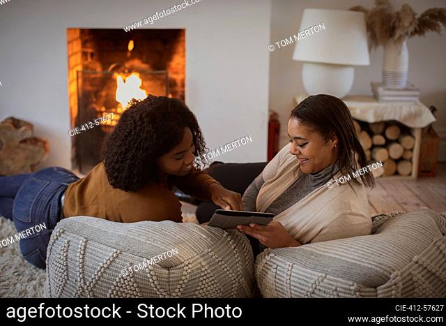 Mother and daughter using digital tablet on poufs at fireplace