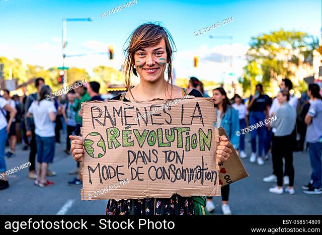 A close up portrait of a young woman during a climate rally on a street, holding a sign saying bring back the revolution of your consumption trend