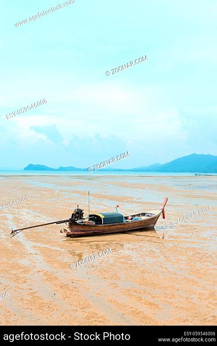 Traditional thai long-tail wooden fishing boat on the deserted sandy sea shore in low-tide time