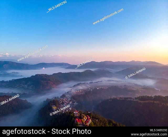 Moody Dramatic view of mountains covered in fog during sunrise with Great Himalaya Range in the backdrop