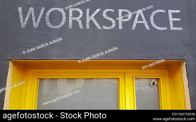 Workspace sign painted over iron yellow door. Banned dogs sticker on right corner
