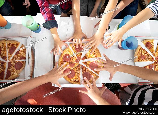 Hands of children reachuing for pizza on table