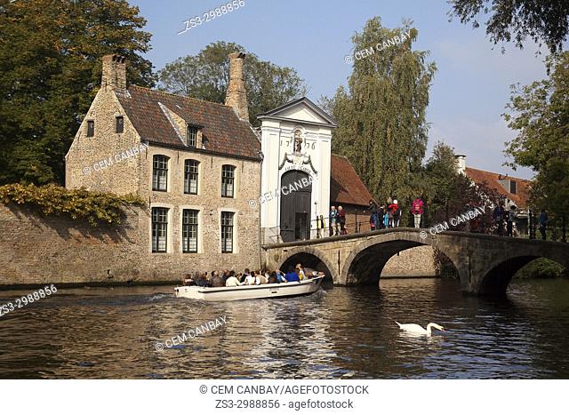 A trip boat on the canal and tourists on the bridge near the Beguinage, Bruges, Belgium, Europe