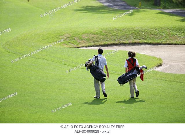 Rear view of a couple walking on the fairway as they carry their golf bags