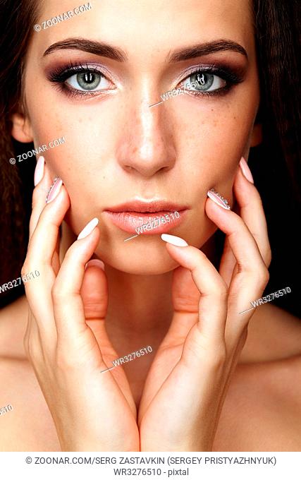 Beauty portrait of young woman touching face with fingers. Brunette girl with long hair and day female makeup
