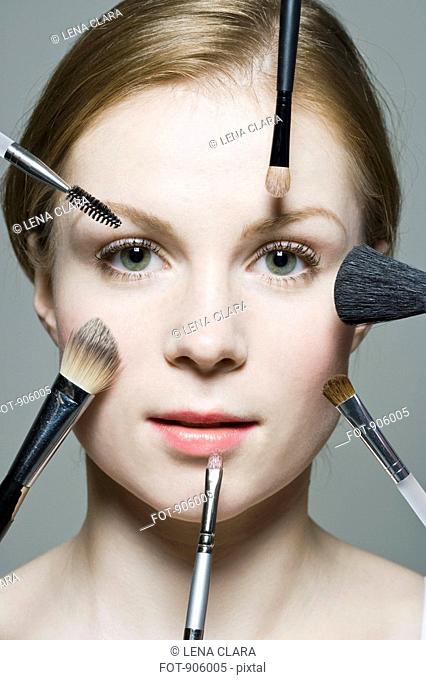 A woman with various make-up brushes applying make-up to her face