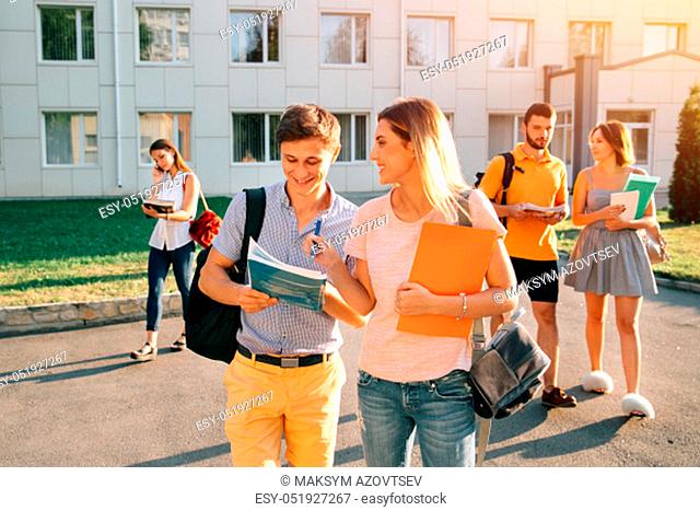 Free time of a students, bachelor`s campus life rhythm. Five friendly students are walking after they passed test outside the college building and discuss the...