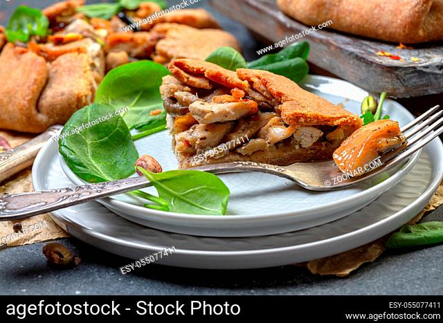 Piece of traditional pie (galete) with chicken, mushrooms, onions served on a plate with fresh spinach and pistachios, selective focus