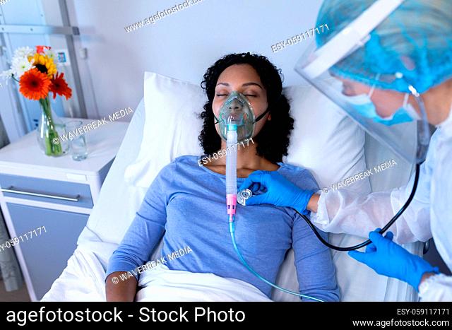 Caucasian doctor in ppe suit examining with stethoscope female patient with ventilator