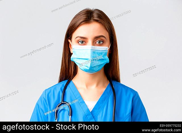 Covid-19, preventing virus, health, healthcare workers and quarantine concept. Close-up young female nurse or doctor in blue scrubs and medical mask looking...