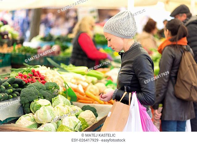 Woman buying fruits and vegetables at local food market. Market stall with variety of organic vegetable