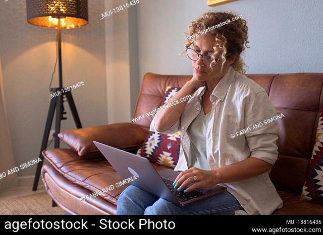 Connected internet people Surfing the net. Thoughtful young woman in eyewear using computer while sitting on the sofa at home - leisure indoor relaxation with...