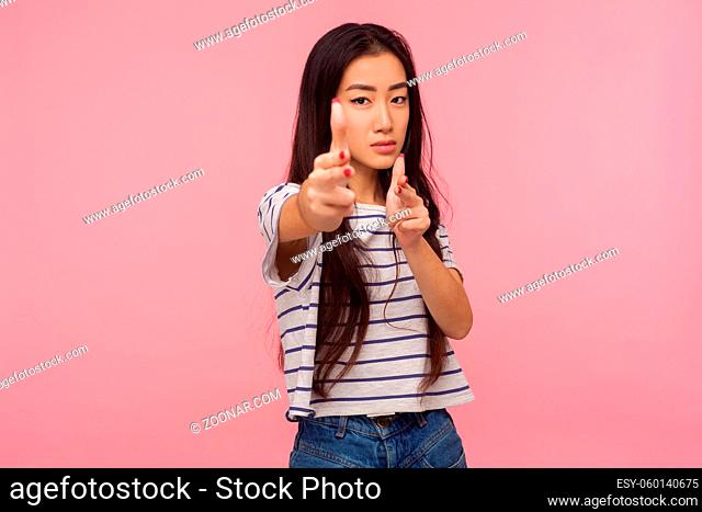 I'll kill you. Serious danger girl with brunette hair in striped t-shirt pointing finger guns to camera and shooting, gesturing weapon, aiming right at target