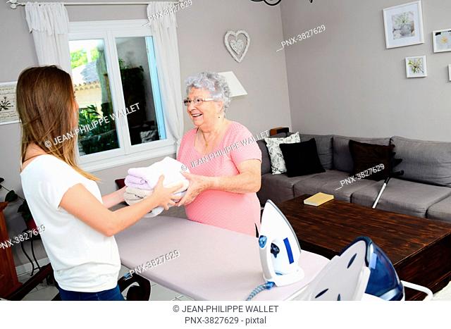 Cheerful young girl ironing and helping with household chores elderly woman at home