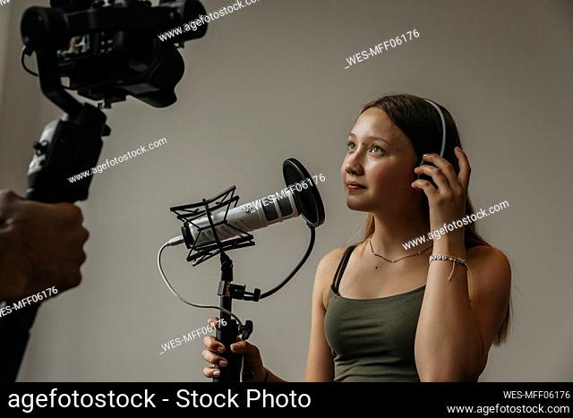 Teenage girl looking at camera while singing over microphone against wall in studio