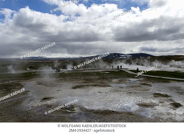 People are walking on boardwalks through the hot springs at Hveravellir, a geothermal area of fumaroles, and multicolored hot pools in the central highlands of...
