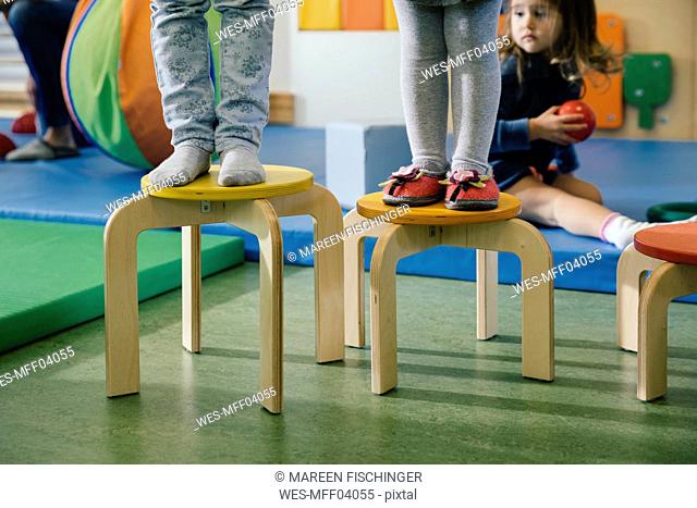 Feet of two children standing on chairs of different heights in kindergarten