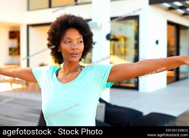 Confident young afro african american woman with arms outstretched exercising in backyard