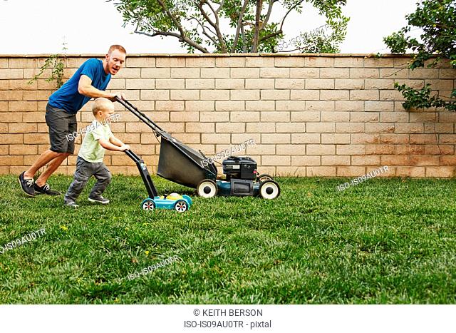 Father and son mowing lawn in backyard