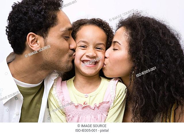 Father and mother kissing daughter on cheek