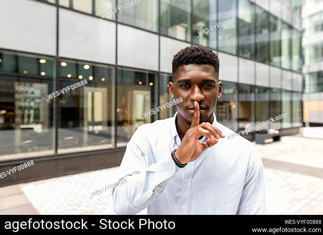 Young man with finger on lips in front of glass building