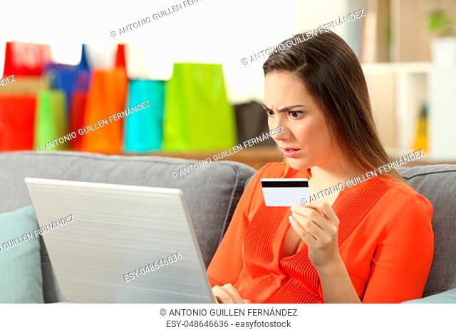 Shocked shopper buying online with credit card sitting on a couch in the living room at home