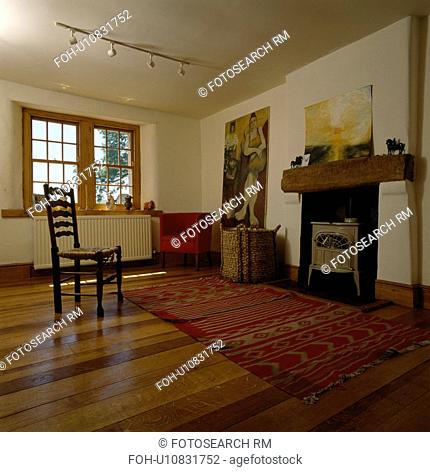 Rush-seated ladderback chair and wooden flooring in sparsely furnished living room with cream stove in fireplace