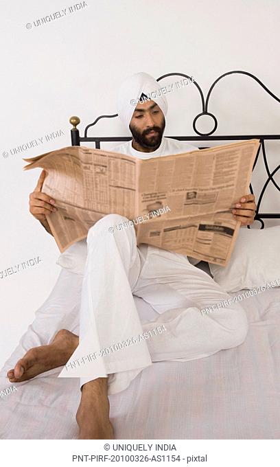 Sikh man reading a newspaper on the bed