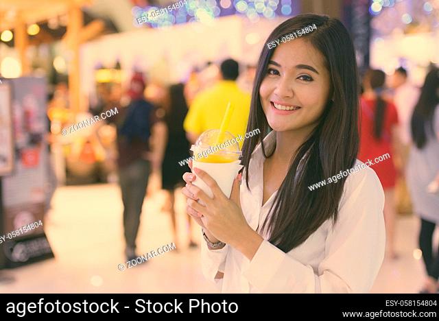 Beautiful Asian woman drinking healthy juice in shopping mall