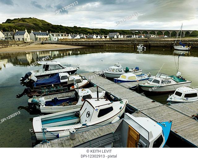 Boats moored in the tranquil harbour of the North Sea with houses in the background; Cullen, Moray, Scotland