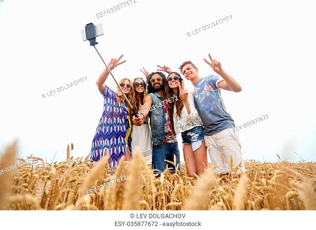 summer, technology and people concept - smiling young hippie friends in sunglasses taking picture by smartphone selfie stick and showing peace sign on cereal...