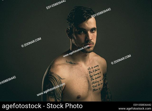 Young handsome man with tattoos and piercings. Fine film grain texture. Studio shot