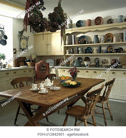 Teaset on wooden table in neutral kitchen with jugs and bowls on shelves above worktop