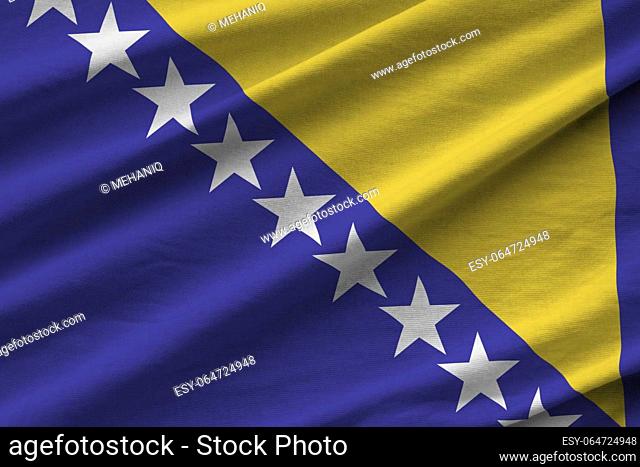 Bosnia and Herzegovina flag with big folds waving close up under the studio light indoors. The official symbols and colors in fabric banner