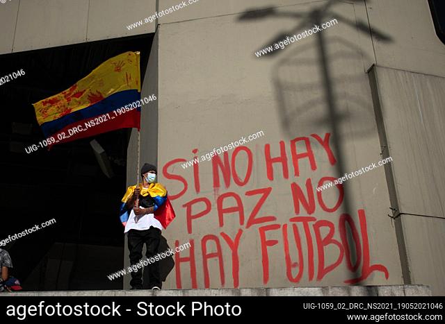Protester waves the Colombian flag while next to him there is a mural that says ""if there is no peace, there is no football"" against the realization of the...