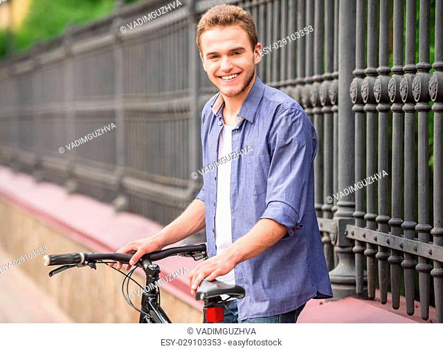 Young beautiful man standing with bicycle at the city street near the fence