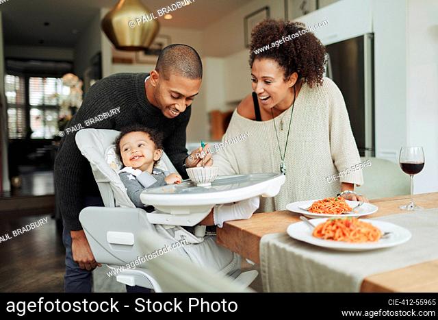 Happy parents feeding baby daughter at dining table