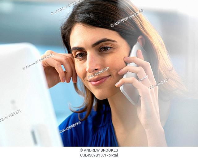 Woman working at computer and using mobile phone in office