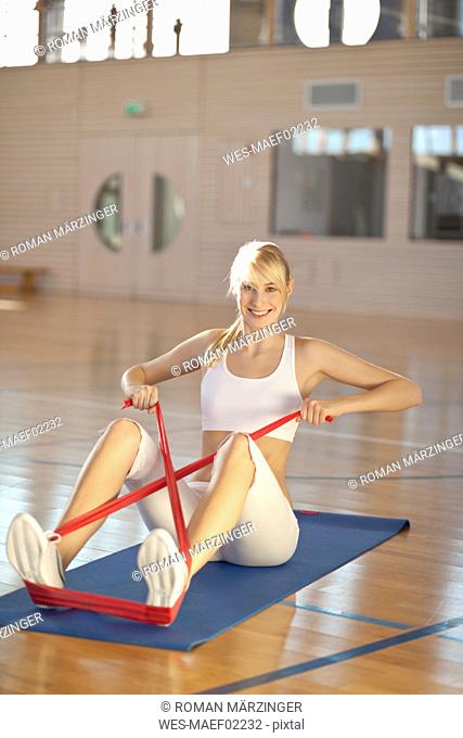 Germany, Mauern, Woman sitting and stretching rubber band, smiling, portrait