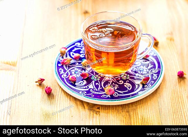 Cup of tea with dry rose buds on wooden table